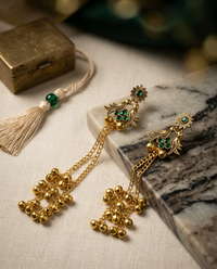 Gold earrings with green gemstones on a marble surface