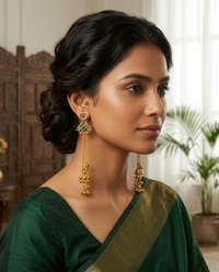 Woman wearing gold earrings with green gemstones, dressed in a green saree, indoors.