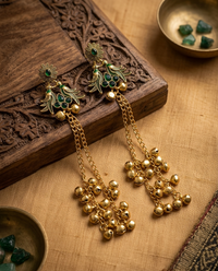 Gold earrings with green gemstones on a wooden surface