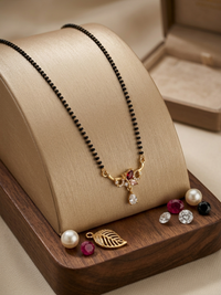 Black beaded necklace with gold and gemstone pendant on a wooden stand