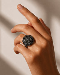 Hand wearing a black textured ring on a neutral background