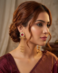 Woman wearing gold earrings with a red gemstone against a neutral background