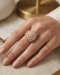 Hand wearing a pearl and diamond ring on a neutral background