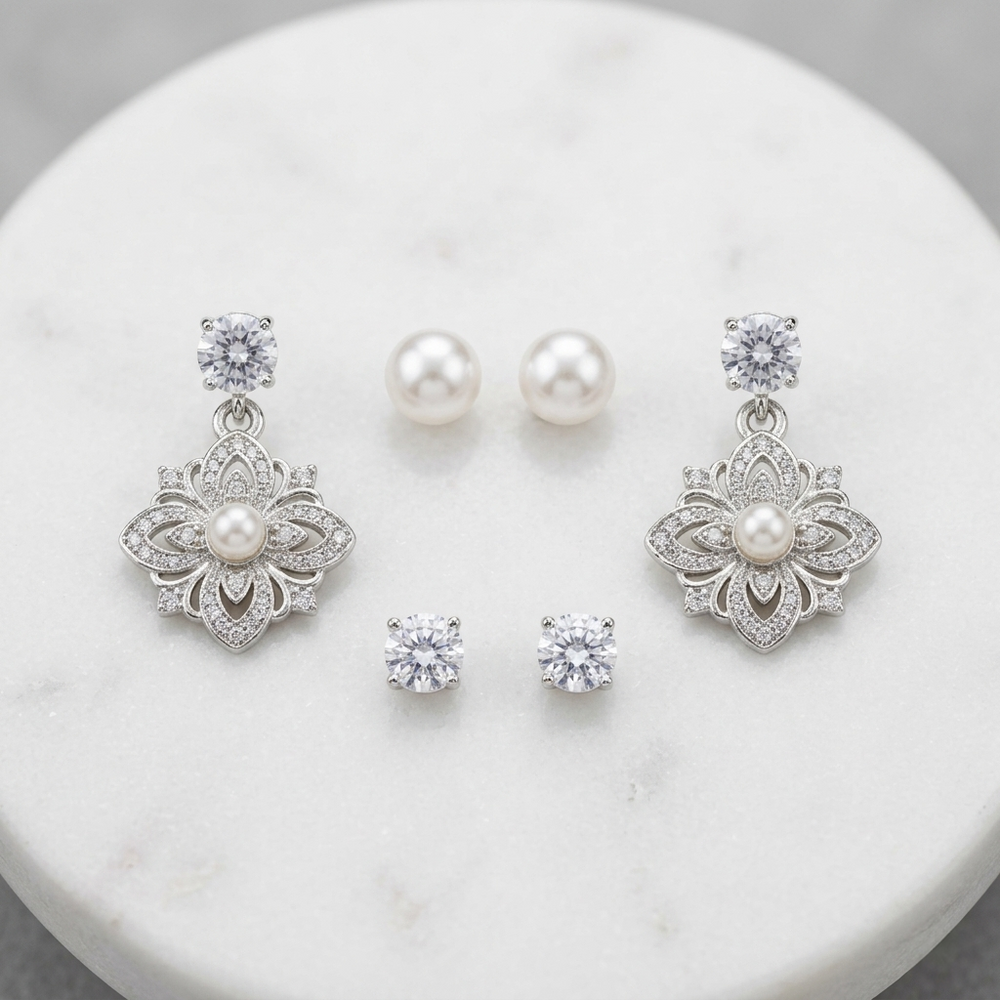 Jewelry set with silver floral earrings and pearl studs on a marble surface