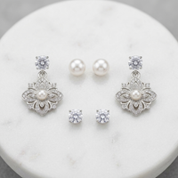 Jewelry set with silver floral earrings and pearl studs on a marble surface