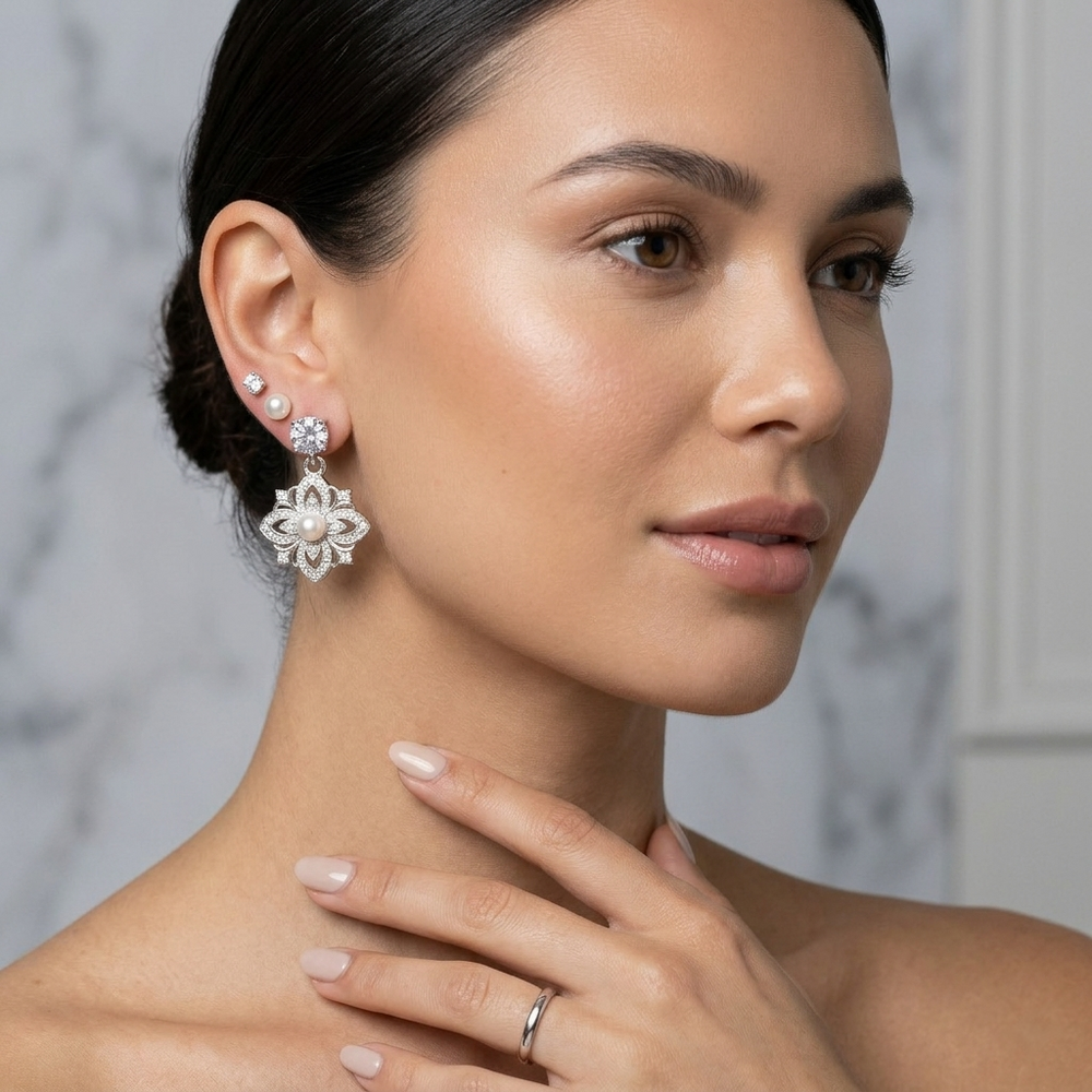 Woman wearing a floral earring with pearls and a ring on a neutral background