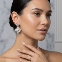 Woman wearing a floral earring with pearls and a ring on a neutral background