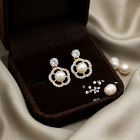 Pearl earrings with silver accents in a brown jewelry box on a beige fabric background