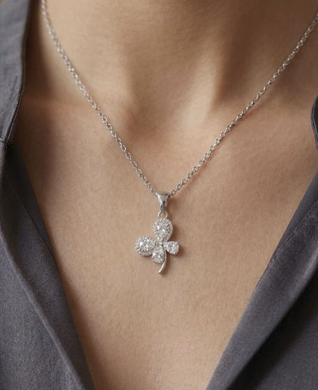 Silver necklace with a clover-shaped pendant worn by a person.