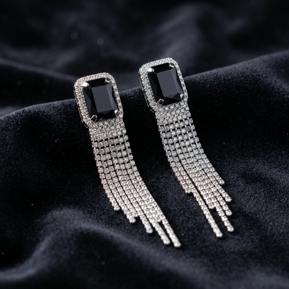 Pair of earrings with black gemstones and silver fringes on a dark fabric background