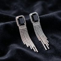 Pair of earrings with black gemstones and silver fringes on a dark fabric background