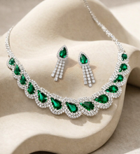 Jewelry set with emerald green stones on a beige stone background