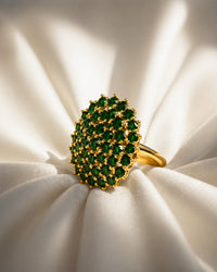 Gold ring with green gemstones on a white fabric background