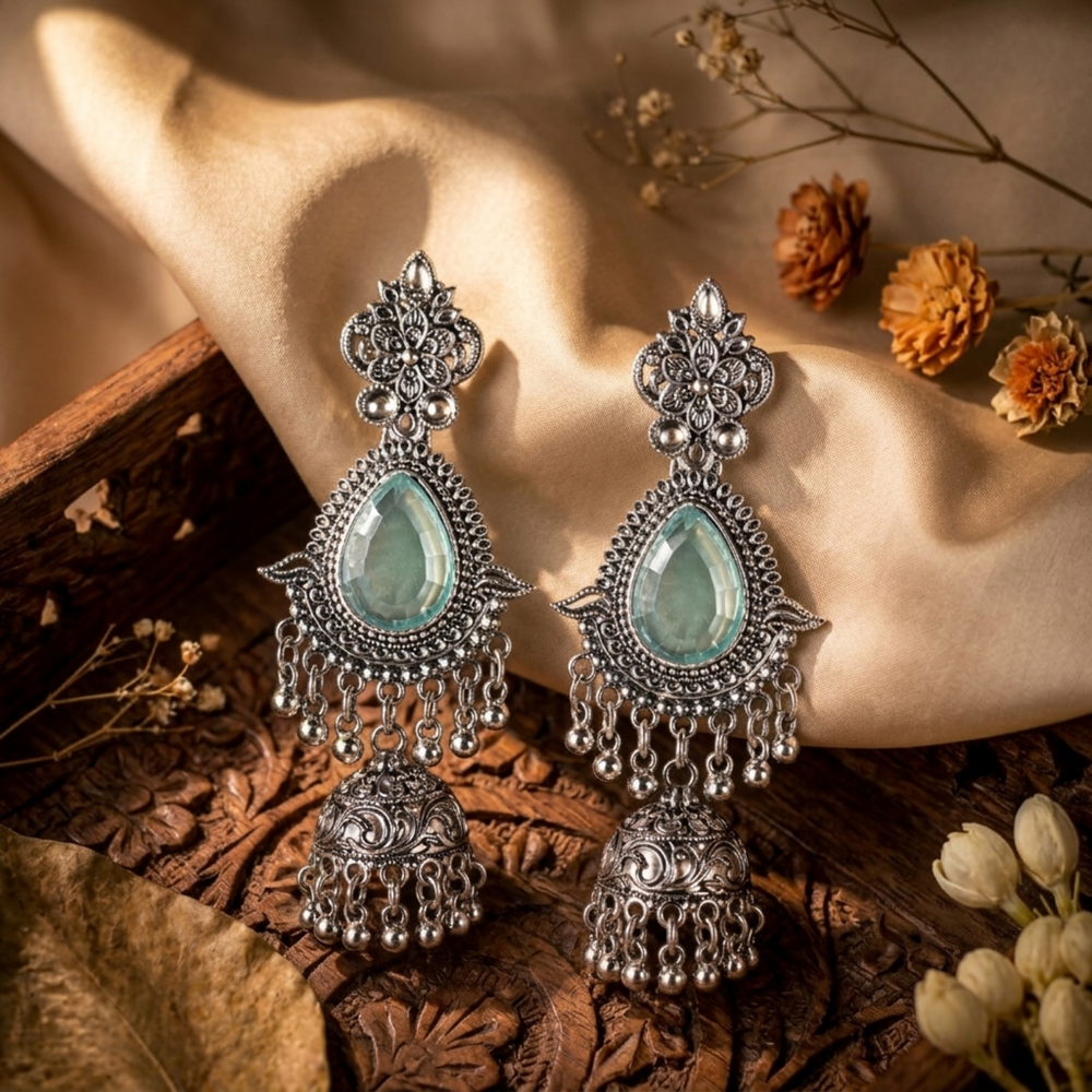 Ornate silver earrings with green gemstones on a decorative surface with flowers.