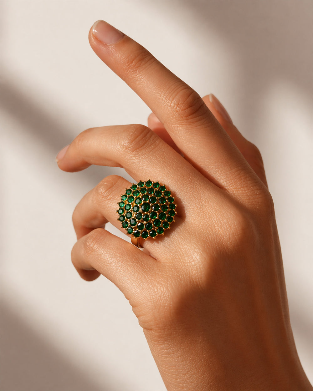 Hand wearing a ring with green gemstones on a neutral background