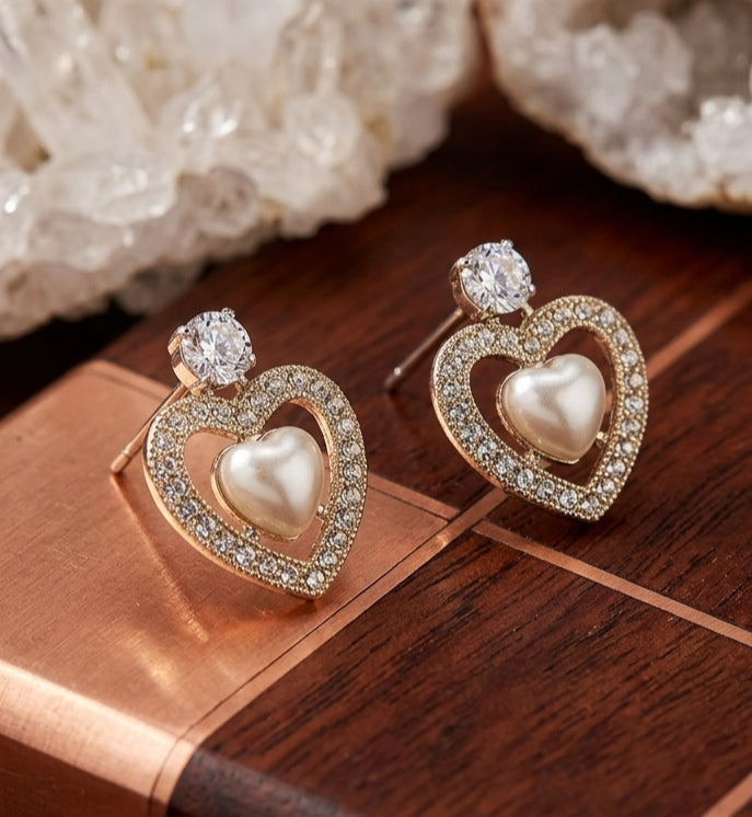 Heart-shaped earrings with pearls and gemstones on a wooden surface.