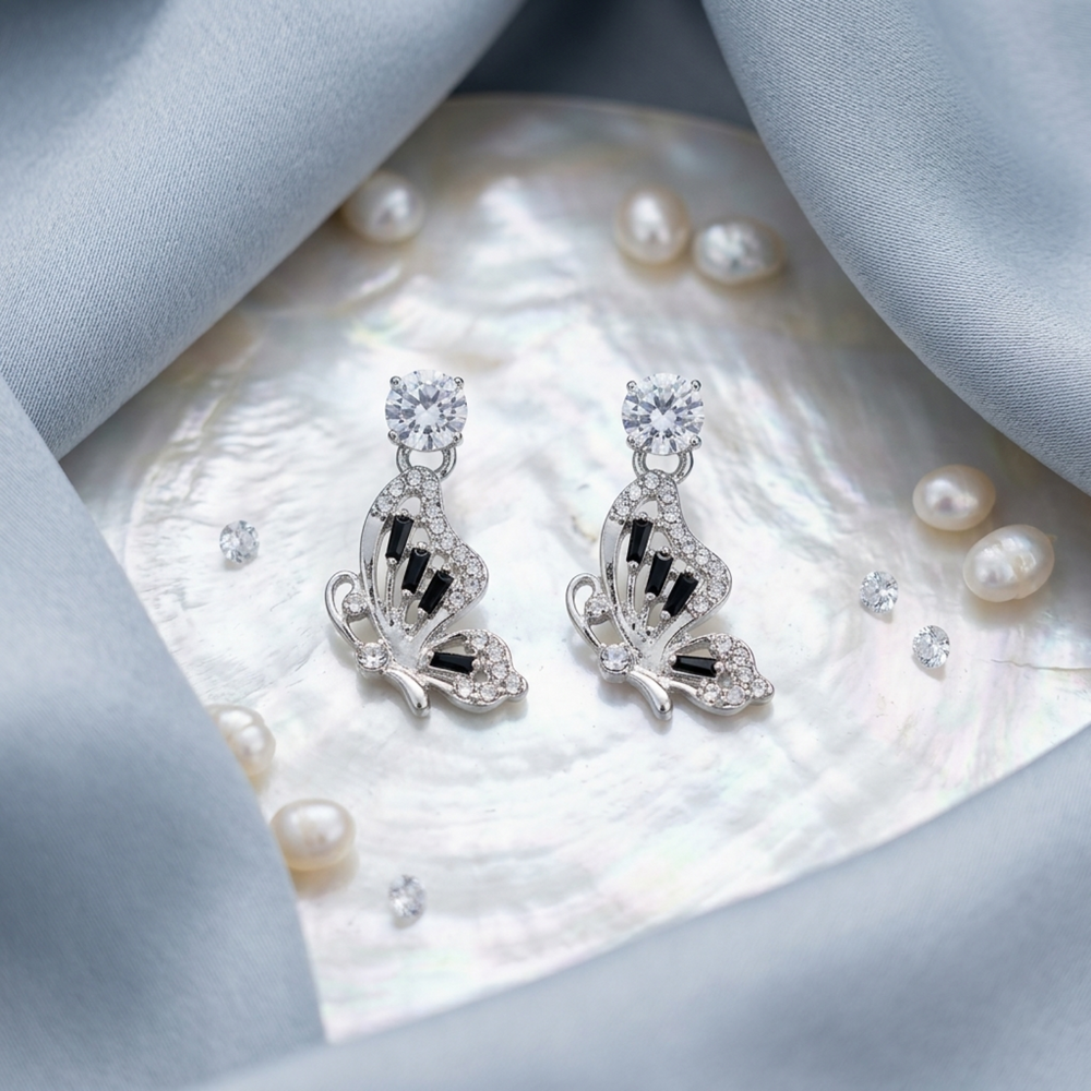 Butterfly-shaped earrings with black accents on a shell with pearls