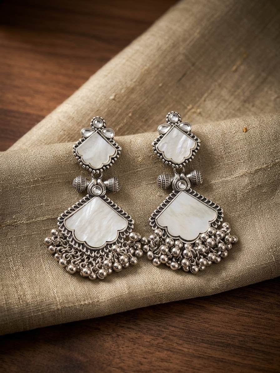 Pair of silver earrings with white stones on a textured fabric surface