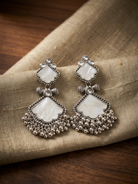 Pair of silver earrings with white stones on a textured fabric surface