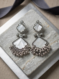 Pair of silver earrings with white stones on a stone surface