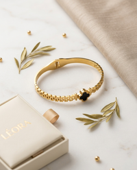Golden color  bracelet with a black heart charm on a marble surface with Léora jewelry box.