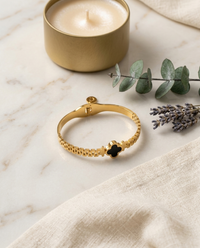 Goldden color bracelet with clover charm on a marble surface with a candle and lavender.