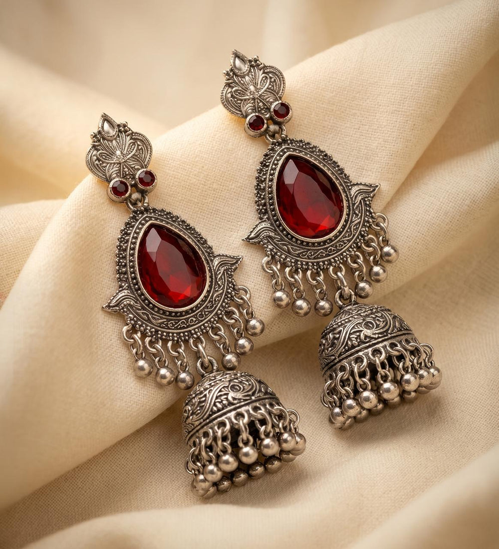 Ornate silver earrings with red gemstones on a beige fabric background