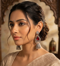 Woman wearing silver earrings with red gemstones against a decorative background
