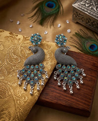 Peacock-shaped earrings with turquoise stones on a decorative surface with peacock feathers.