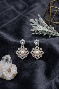 Pair of silver floral earrings with pearls on a dark fabric background