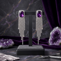 Purple gemstone earrings on a black stand with amethyst crystals in the background