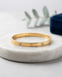 Gold bracelet with embedded stones on a marble surface with a light background