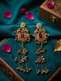 Gold earrings with red gemstones on a blue fabric background with rose petals.