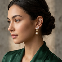 Woman wearing gold earrings with a pearl accent against a neutral background