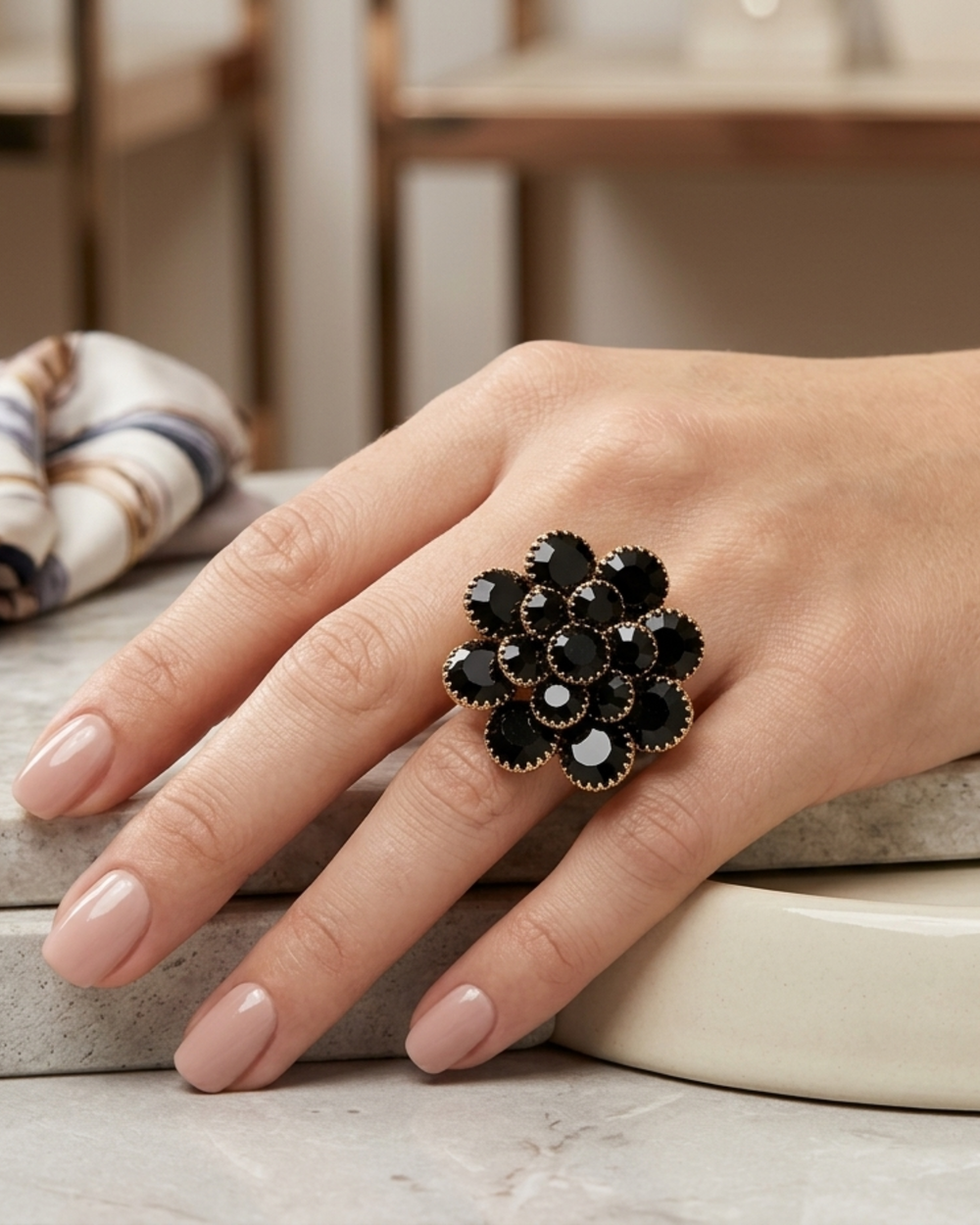 Close-up of a hand wearing a black floral ring on a neutral background