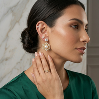 Woman wearing a pair of earrings and a ring, with a neutral background