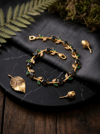Gold bracelet with green stones on a dark surface with leaves
