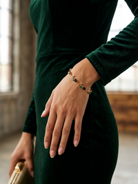 Person wearing a green dress with a bracelet, holding a gold clutch.