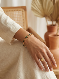 Hand wearing a gold ring and bracelet with a neutral background