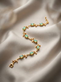 Gold bracelet with green gemstones on a satin surface