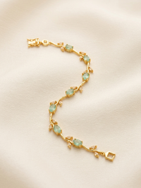 Gold bracelet with green gemstones on a beige background