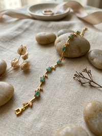 Gold bracelet with green stones on a textured surface with stones and dried plants