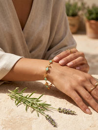 Person wearing a gold bracelet with turquoise stones on a sandy surface with plants in the background