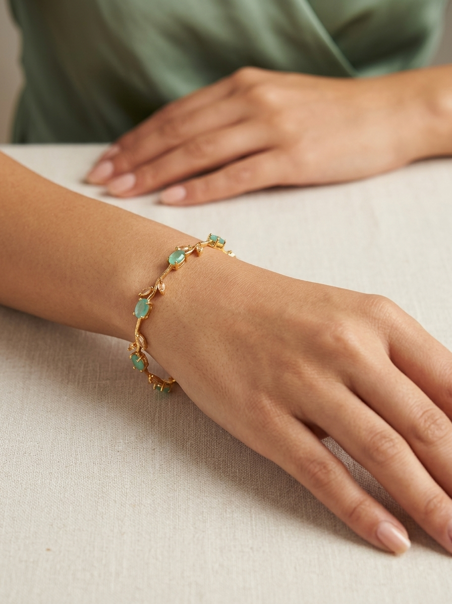 Gold bracelet with green gemstones on a wrist against a neutral background