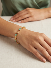 Gold bracelet with green gemstones on a wrist against a neutral background