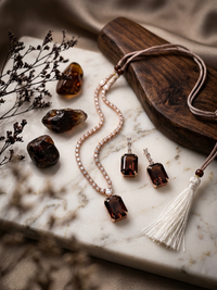 Jewelry set with necklaces and earrings on a marble surface with amber stones and a wooden box.