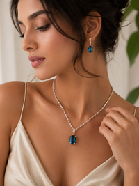 Woman wearing a diamond necklace and earrings with a blue gemstone.
