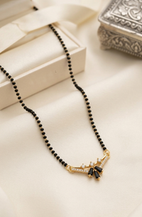 Black beaded necklace with a gold and black pendant on a beige surface