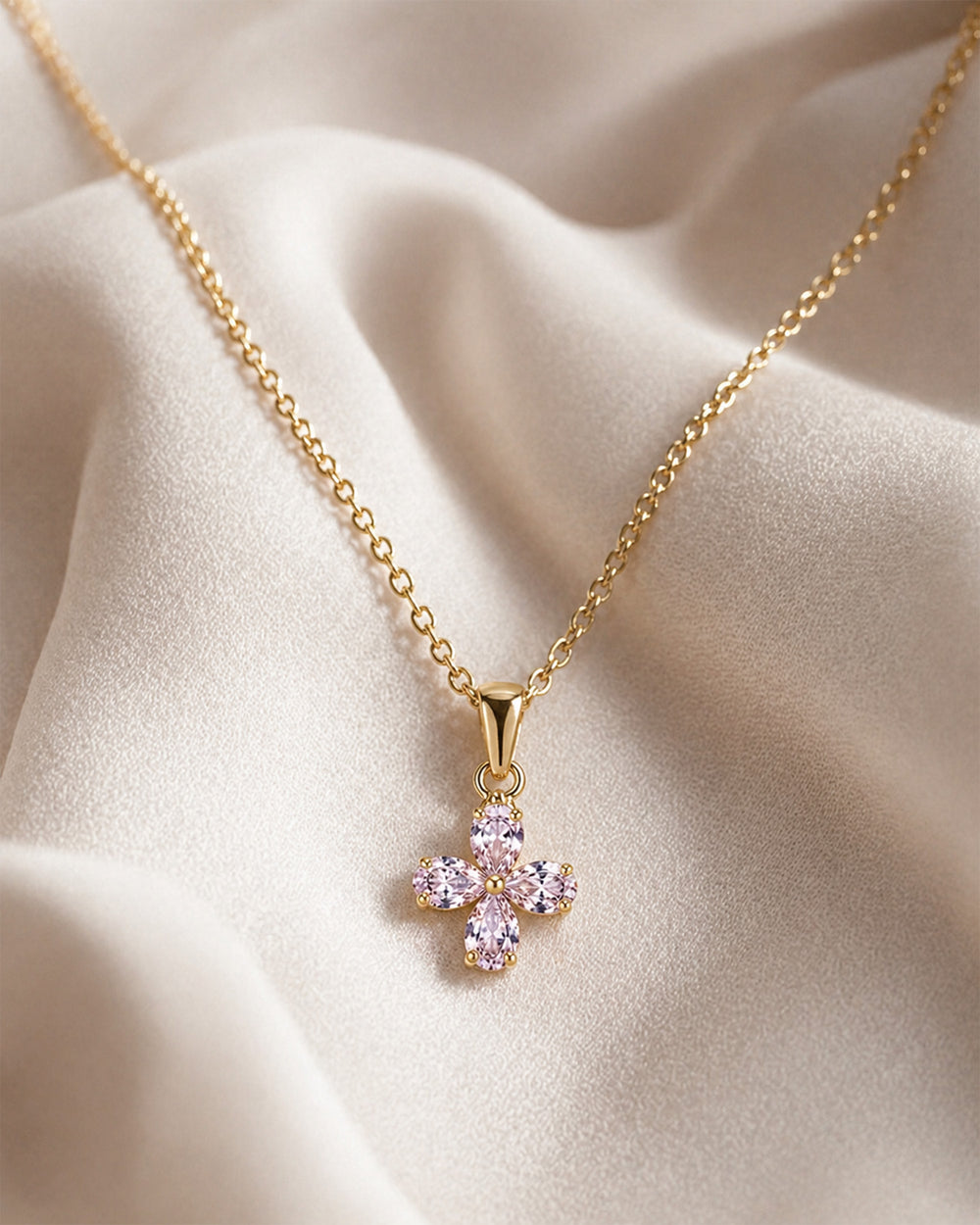 Gold necklace with a pink flower pendant on a beige fabric background