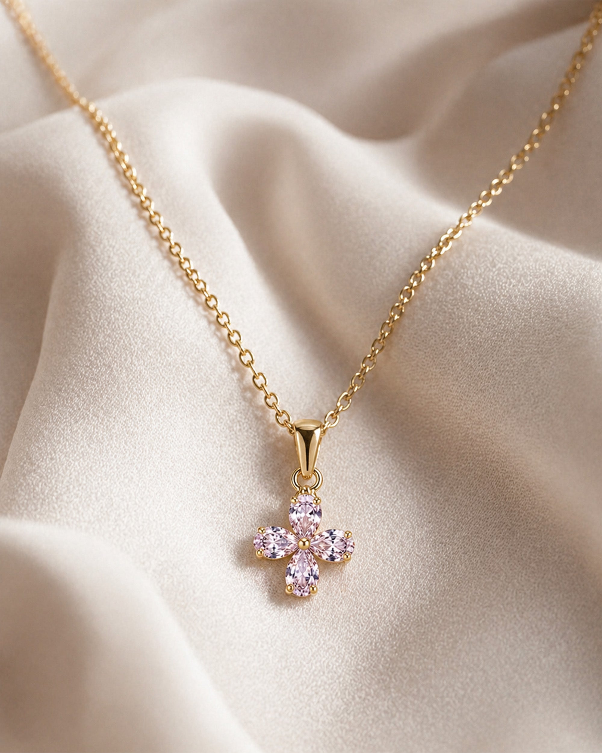 Gold necklace with a pink flower pendant on a beige fabric background